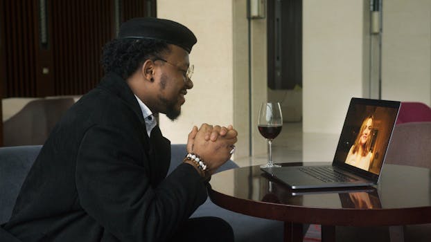 A man video calling on laptop with wine, indoors setting perfect for dating.