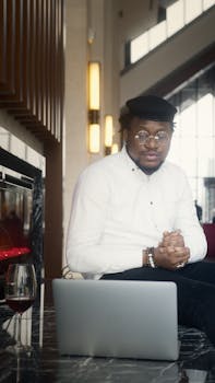 A stylish young man sitting by a laptop in a modern cafe setting, exuding confidence.