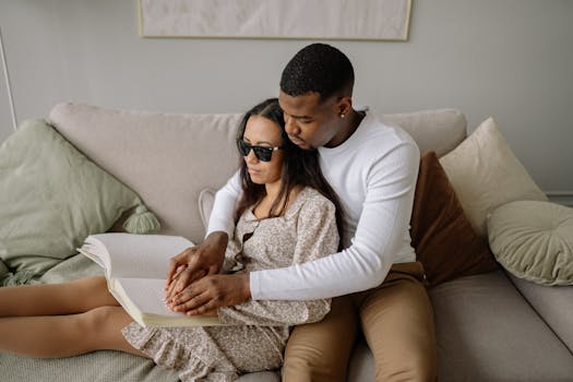 Couple embracing on a sofa, reading a braille book together, symbolizing love and inclusivity.