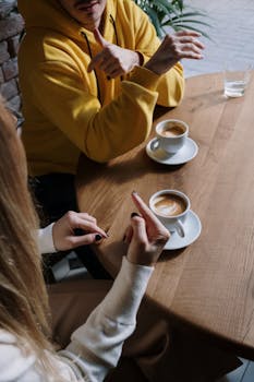 Two people using sign language over coffee in an intimate indoor setting.